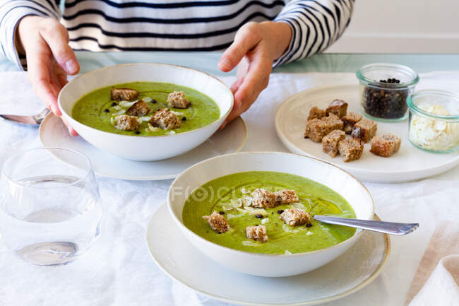 Alto angolo di coltura persona irriconoscibile seduto a tavola e mangiare appetitosa zuppa di crema di zucchine per il pranzo — Foto stock