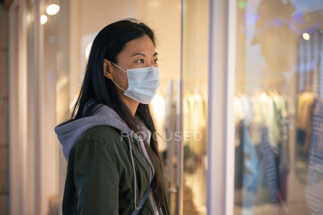 Vista laterale ragazza asiatica indossa una maschera di fronte al negozio di abbigliamento — Foto stock