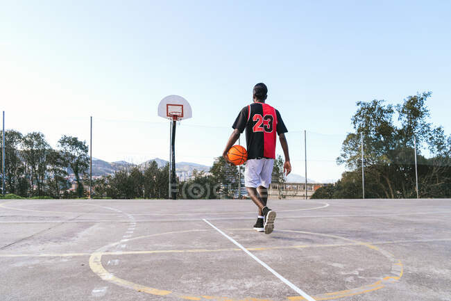 Visão traseira de jogador de streetball masculino afro-americano irreconhecível em uniforme com bola na quadra de basquete — Fotografia de Stock