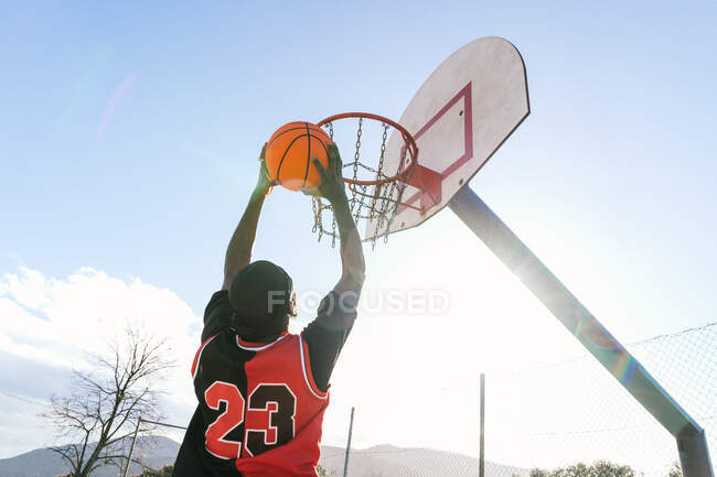 From below of African American male streetball player in moment of jumping and scoring basketball in hoop — Stock Photo