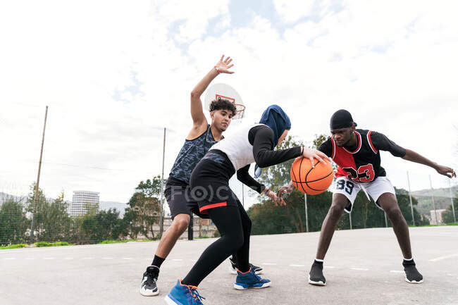 Мультиэтнические друзья летом играют в уличный баскетбол на спортивной площадке — стоковое фото
