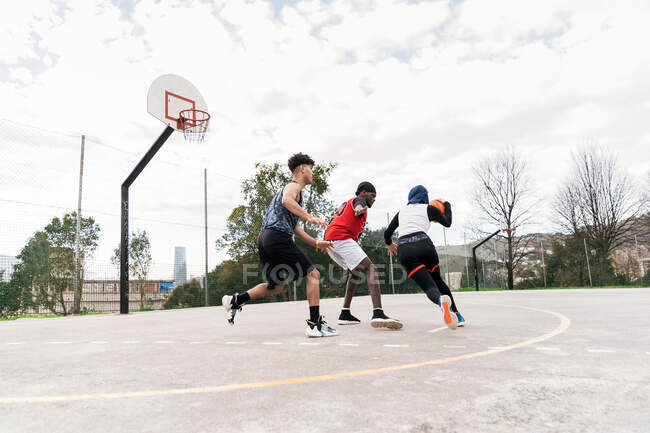 Amis multiethniques jouant au basket de rue sur un terrain de sport en été — Photo de stock