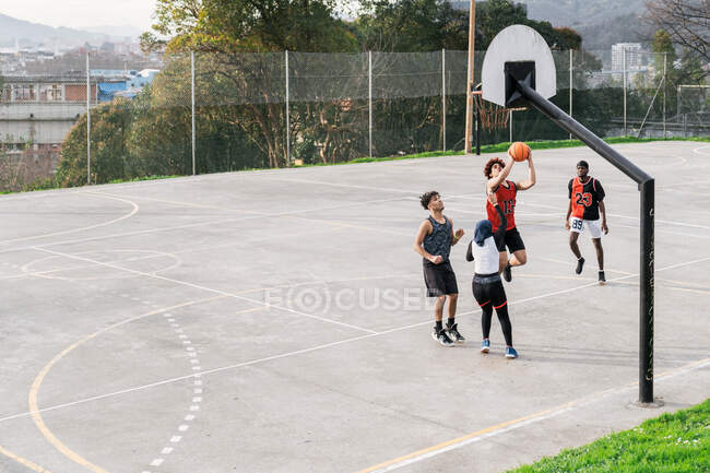 Alto ángulo de amigos multiétnicos jugando baloncesto callejero en el campo de deportes en verano - foto de stock