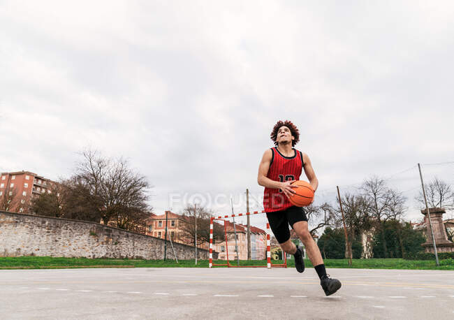 Determined African American male streetball player playing basketball on sports ground in summer — Stock Photo