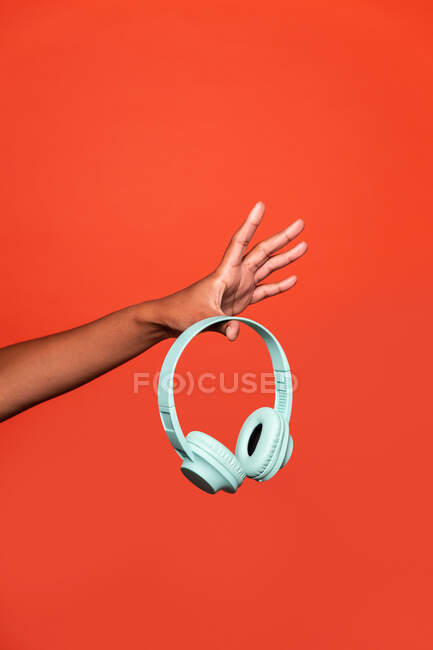 Crop anonymous African American female showing wireless headphones on outstretched hand against red background in studio — Stock Photo
