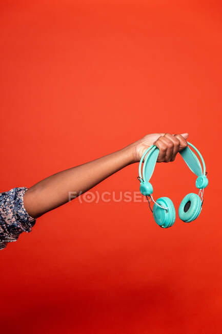 Ernte anonyme Afroamerikanerin zeigt drahtlose Kopfhörer auf ausgestreckter Hand vor rotem Hintergrund im Studio — Stockfoto