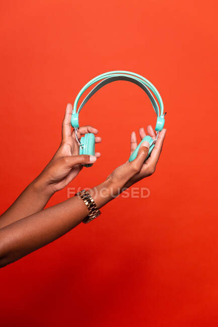 Ernte anonyme Afroamerikanerin zeigt drahtlose Kopfhörer auf ausgestreckter Hand vor rotem Hintergrund im Studio — Stockfoto