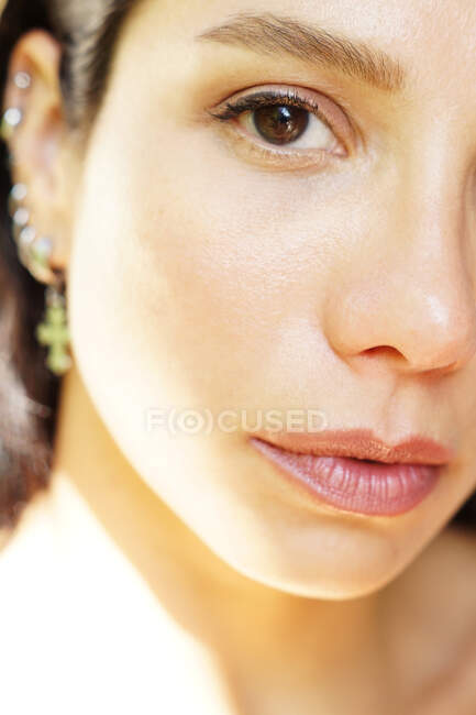 Crop young tender female in earrings with sensitive lips looking at camera on sunny day — Stock Photo