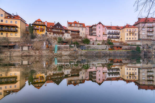 Pintoresca vista de viejos edificios residenciales en mal estado que reflejan en aguas tranquilas del río - foto de stock