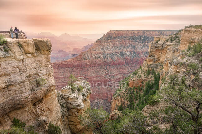 Casal de viajantes em pé na rocha e admirando paisagens espetaculares do Grand Canyon National Park sob o céu do pôr-do-sol no Arizona — Fotografia de Stock