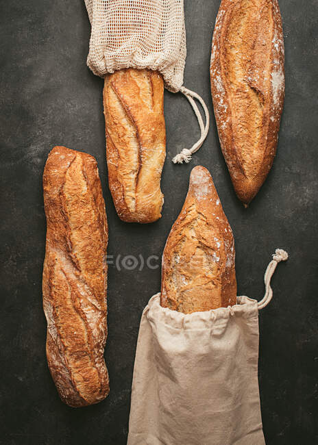 Composición de vista superior de deliciosos panes de masa fermentada artesanal crujientes envasados en bolsas de arpillera sobre fondo negro - foto de stock