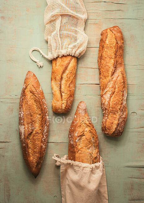 Composición de vista superior de deliciosos panes de masa fermentada artesanal crujientes envasados en bolsas de arpillera sobre fondo verde - foto de stock