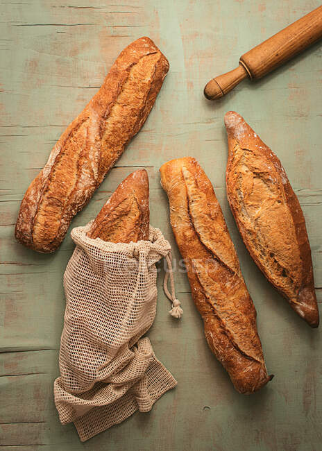 Top view composition of delicious crispy artisan sourdough bread loaves packed in burlap bags on green background — Stock Photo