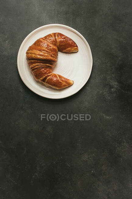 Top view composition with appetizing freshly baked crusty croissant served on white and black plate on table — Stock Photo