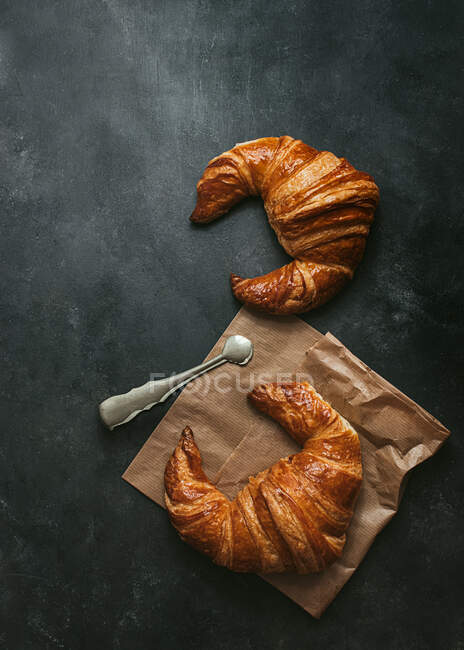 Zusammensetzung von oben mit leckeren frischen Croissants mit Papiertüte und Metallzange auf schwarzem Hintergrund — Stockfoto