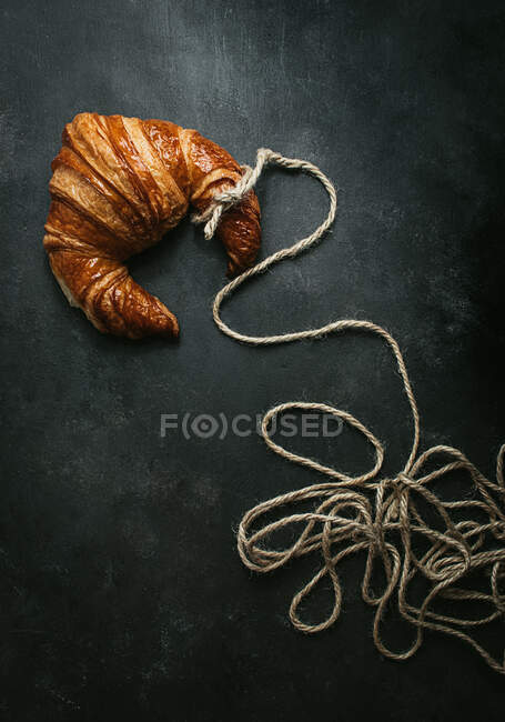 From above of delicious freshly baked traditional croissant wrapped with rope on black background — Stock Photo
