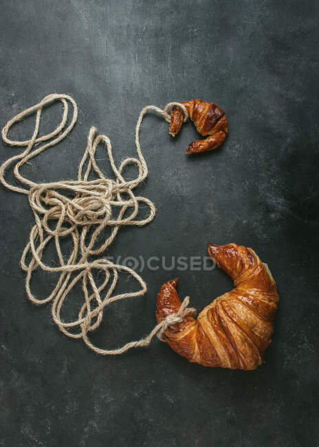 Von oben köstliche frisch gebackene traditionelle Croissant mit Seil auf schwarzem Hintergrund gewickelt — Stockfoto