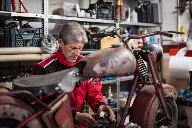 Mecânico masculino sênior reparando a velha moto enferrujada desmontada enquanto trabalhava em oficina profissional — Fotografia de Stock