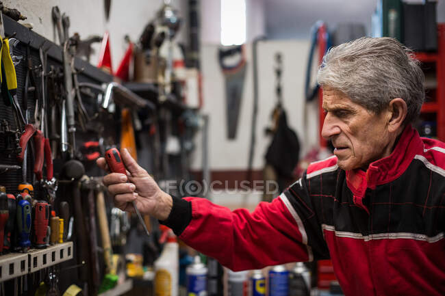 Side view of aged skilled repairman taking professional tools from rack while working in service workshop — Stock Photo
