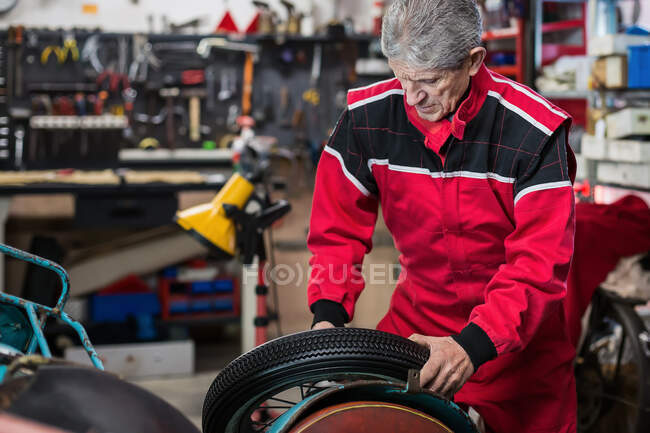 Réparateur senior sérieux roue de fixation de la vieille moto tout en travaillant dans un atelier de service professionnel — Photo de stock
