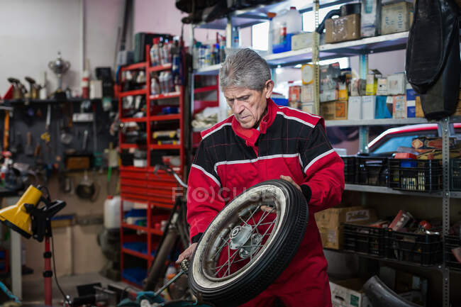 Серьезный старший ремонтник чинит колесо старого мотоцикла во время работы в мастерской профессионального сервиса — стоковое фото