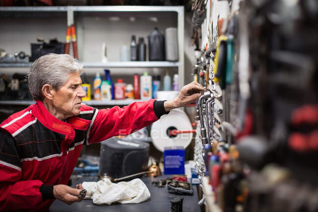 Seitenansicht eines gealterten gelernten Reparateurs, der während seiner Arbeit in der Werkstatt professionelle Werkzeuge aus dem Regal holt — Stockfoto