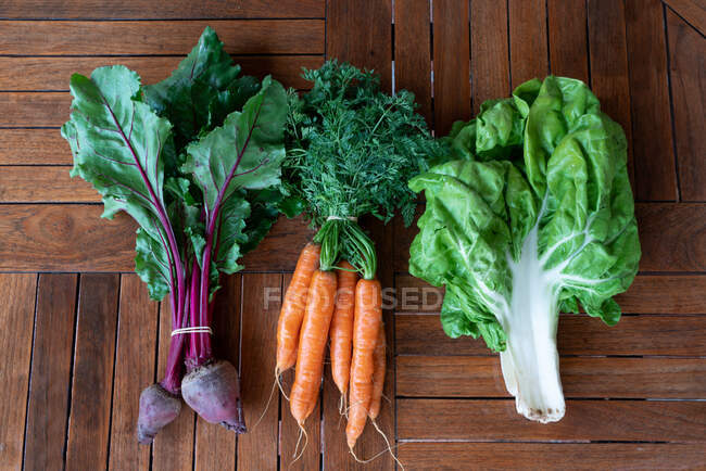 From above of bunches of ripe beet and carrot placed on wooden table near green chard leaves in countryside — Stock Photo