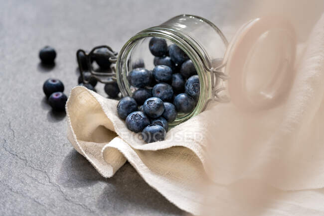Haufen frischer reifer Blaubeeren aus Glas auf Serviette auf grauem Tisch im Atelier verstreut — Stockfoto