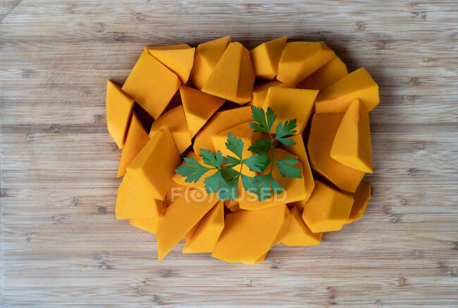 Top view of pile of pieces of ripe pumpkin garnished with fresh sprig of parsley placed on wooden table — Stock Photo