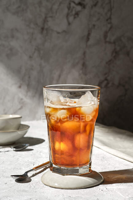 Glas erfrischenden kalten Tee mit Eiswürfeln, serviert auf Glas auf Tisch mit Löffel im Sonnenlicht — Stockfoto