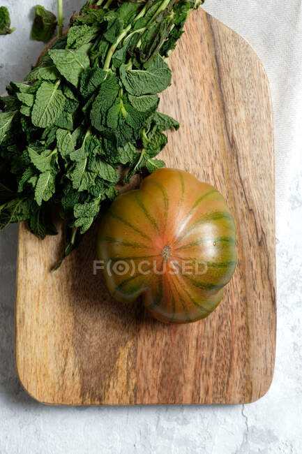 From above of fresh striped green and red tomato placed on wooden cutting board with bunch of mint stems — Stock Photo