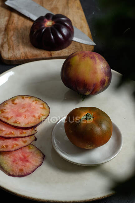 Зверху свіжі цілі і нарізані чорні помідори на столі під час приготування здорової їжі — стокове фото