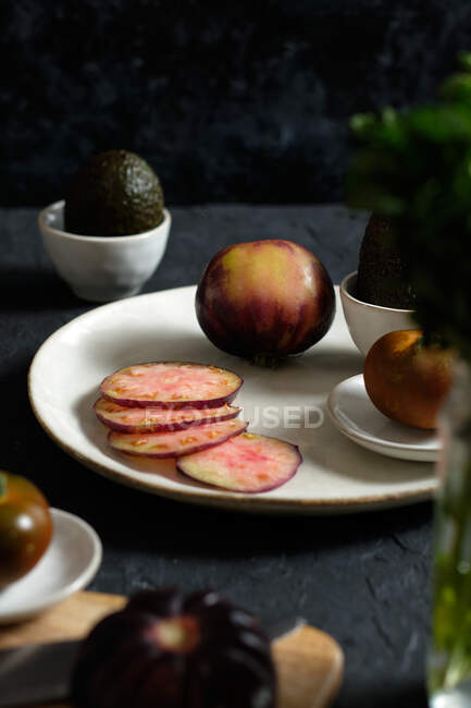 Dall'alto di pomodori neri freschi interi e affettati sul tavolo con avocado e menta verde durante la preparazione di pasti sani — Foto stock