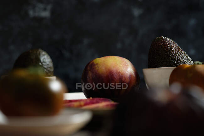 Pomodori neri freschi interi e affettati in tavola con avocado durante la preparazione di pasti sani — Foto stock