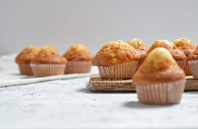 Délicieux muffins sucrés maison fraîchement cuits dans des tasses en papier disposées sur la table — Photo de stock