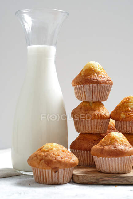 Deliziosi muffin dolci fatti in casa appena sfornati in bicchieri di carta disposti sul tavolo con barattolo di vetro di latte fresco — Foto stock