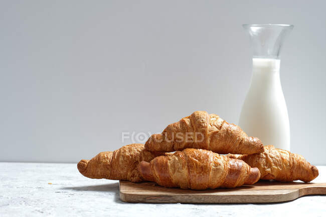 Deliciosos croissants e garrafa de leite colocados na mesa para o café da manhã na cozinha — Fotografia de Stock