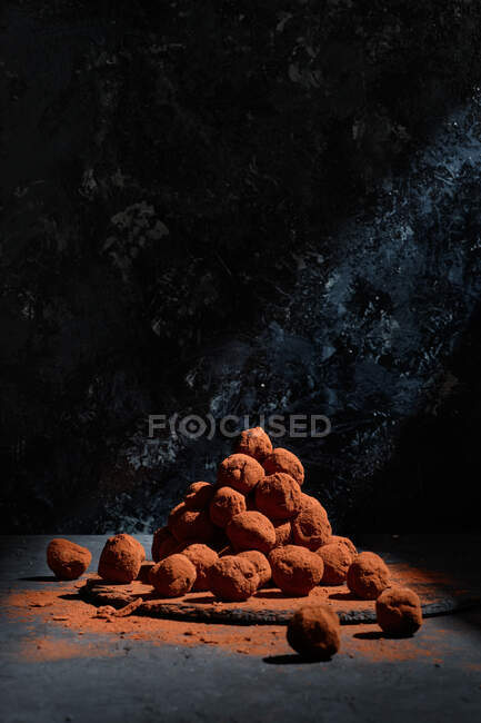 Haufen köstlicher Schokoladentrüffel in Kugelform stapeln sich auf dem Tisch vor dunklem Hintergrund im Atelier — Stockfoto