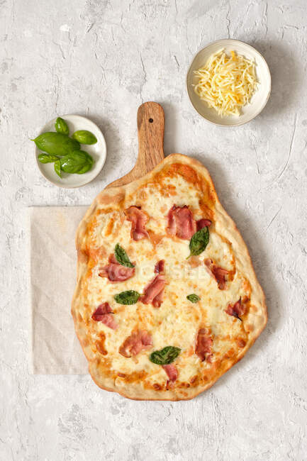 D'en haut de savoureuse pizza maison au basilic et jambon servi sur une planche à découper en bois sur table — Photo de stock
