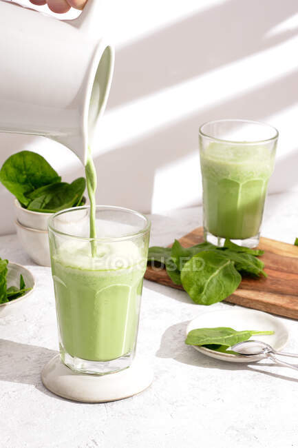 Unrecognizable person pouring healthy spinach smoothie in glass placed on table for breakfast at home — Stock Photo