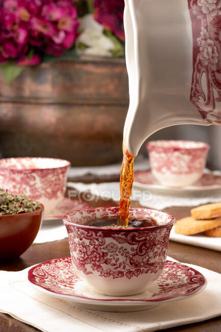 Chá quente aromático sendo derramado em copo de cerâmica colocado na mesa para o café da manhã em casa — Fotografia de Stock