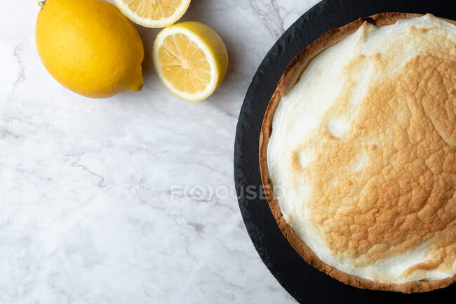 Vista superior da torta de merengue apetitosa servida na mesa de mármore com limões frescos na cozinha — Fotografia de Stock