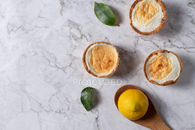 Top view of yummy homemade meringue tarts placed on table with fresh lemon and green leaves — Stock Photo