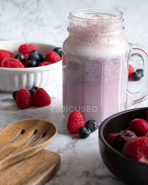 Frullato di frutti di bosco rinfrescante in tazza di vetro posto sul tavolo con lamponi e mirtilli per una colazione sana — Foto stock