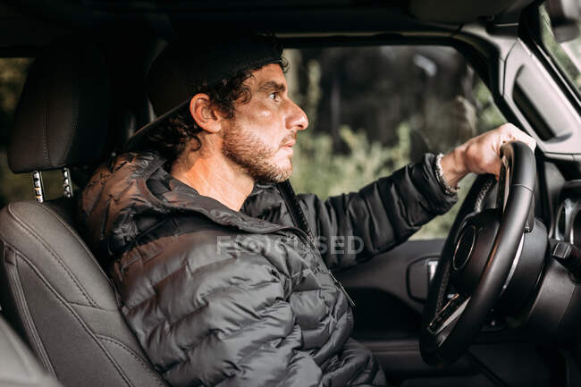 Side view of bearded man driving car on blurred background at sunset — Stock Photo