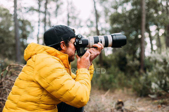 Вид сбоку на фотографа-авантюриста, делающего фотографии в горах на размытом фоне — стоковое фото