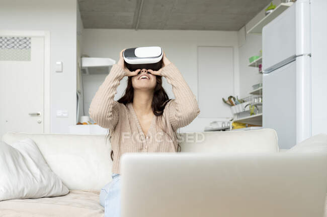 Anonyme Content-Frau erkundet virtuelle Realität im Headset, während sie auf dem Sofa im Hauszimmer sitzt — Stockfoto