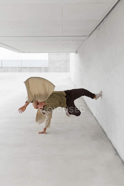 Male dancer balancing on arm and showing breakdance movement while leaning on concrete wall of building in city — Stock Photo