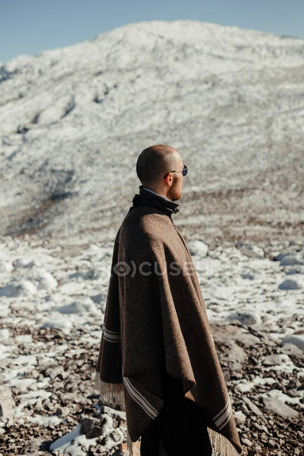 Турист на мысе с видом на снежную гору под голубым облачным небом зимой — стоковое фото