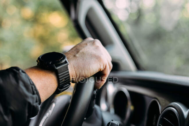Crop view of anonymous man with her hand on a car steering wheel on blur background — Stock Photo